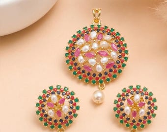Può includere: Un set di gioielli color oro composto da un ciondolo circolare e orecchini abbinati. Ogni pezzo presenta una disposizione centrale di perle bianche e pietre rosa taglio marquise, circondate da anelli di piccole pietre rotonde verdi e blu.