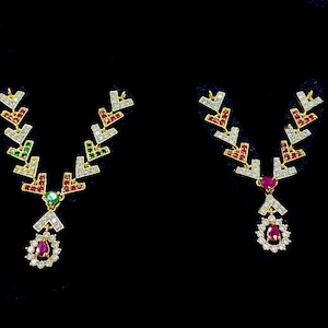 May include: Two gold necklaces with red, green and white gemstones. The necklaces are on a black background.