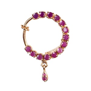 May include: Gold nose ring with a teardrop pendant. The ring is decorated with a row of pink gemstones.