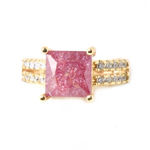 May include: A gold ring with a square pink gemstone and clear stones on the band.