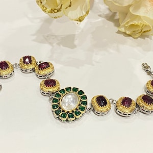 Peut inclure: Un bracelet en or et argent avec une grande pierre centrale de forme ovale entourée de pierres vertes. Le bracelet est orné de plus petites pierres rouges serties d'or.
