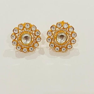 May include: A pair of gold earrings with a circular design. The earrings are adorned with clear stones and have a central round stone.