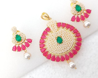 Può includere: Un set di gioielli color oro con un ciondolo e orecchini abbinati. Il ciondolo e gli orecchini hanno una gemma verde centrale, circondata da piccole perle bianche e pietre rosa a forma di goccia. Ogni orecchino e il ciondolo hanno una perla bianca pendente.