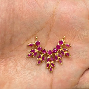May include: A gold-toned jewelry connector featuring a fan-shaped arrangement of vibrant pink, marquise-cut stones. The piece has two small loops at the top for attachment and a symmetrical design with multiple leaf-like gemstone settings.
