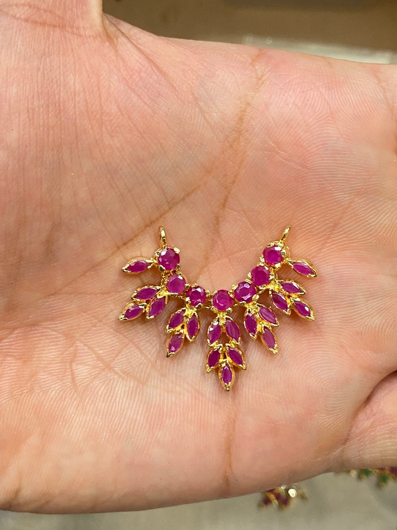 May include: A gold-toned jewelry connector featuring a fan-shaped arrangement of vibrant pink, marquise-cut stones. The piece has two small loops at the top for attachment and a symmetrical design with multiple leaf-like gemstone settings.