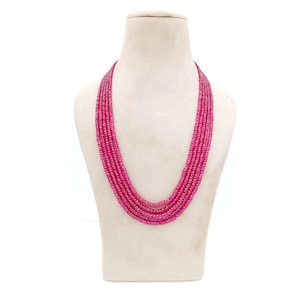 May include: A multi-strand necklace displayed on a mannequin. The necklace is composed of numerous small, round, magenta-colored beads. The strands cascade in a gentle curve, creating a layered effect. The background is plain white.