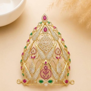 Può includere: Un copricapo color oro caratterizzato da un intricato design in filigrana decorato con numerosi cristalli pavé trasparenti, pietre rosa a forma di goccia e piccole pietre verdi. Il pezzo è etichettato DESIGN A e ha una sagoma a punta.