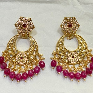 May include: A pair of gold earrings with a pink and white floral design and a dangling row of pink beads.