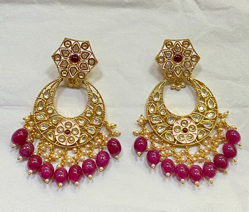 May include: A pair of gold earrings with a pink and white floral design and a dangling row of pink beads.