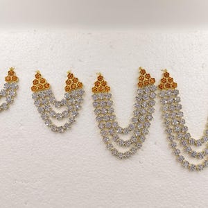May include: Four decorative jewelry pieces featuring a U-shaped design with multiple strands of clear, round, faceted stones. Each piece has a triangular top section adorned with small, amber-colored stones set in a gold-toned metal frame.