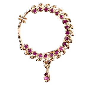 Puede incluir: Un aro de nariz de oro con un colgante en forma de lágrima y una fila de piedras preciosas púrpuras engastadas en diseños en forma de paisley.