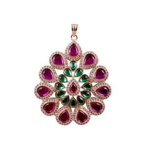 May include: A gold pendant with a circular design featuring pink and green gemstones. The pendant is surrounded by smaller clear gemstones.
