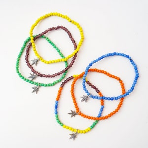 May include: Five colourful beaded bracelets with silver star charms. The bracelets are layered in a rainbow pattern, with yellow, green, purple, blue, and orange beads.