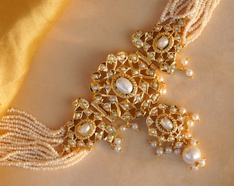 May include: A gold necklace with a large, ornate pendant featuring a pearl center and intricate detailing. The necklace is made of multiple strands of small white pearls.