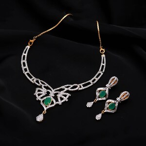 Peut inclure: Un ensemble de bijoux composé d'un collier et de boucles d'oreilles pendantes assorties. Le collier présente une chaîne dorée avec une pièce centrale argentée ornée de cristaux clairs et d'une pierre ovale verte, avec une breloque en cristal.