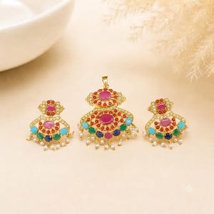 May include: A gold-toned jewelry set consisting of a pendant and two matching earrings. Each piece features a central oval pink stone surrounded by smaller red, turquoise, green, and blue stones, accented with tiny white beads along the edges.