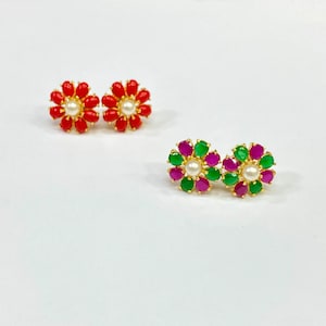 May include: Two pairs of flower-shaped earrings. One pair has red stones and a white pearl in the center. The other pair has green and pink stones with a white pearl in the center.
