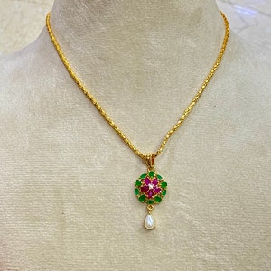 May include: A gold chain necklace with a pendant featuring a round cluster of green and pink gemstones, with a single pearl drop hanging below.
