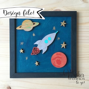 May include: A framed wooden artwork with a blue background depicting a rocket ship, a planet with rings, a red planet, and gold stars. The artwork has a black frame.