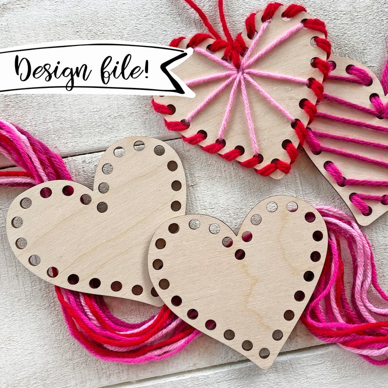 May include: Three unfinished wooden heart-shaped embroidery projects with pink and red yarn. The yarn is threaded through pre-drilled holes in the wood. The text "Design file!" is written on a white banner.