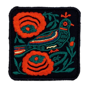 Puede incluir: Parche bordado con un pájaro turquesa, flores naranjas y hojas verdes sobre un fondo negro. El pájaro tiene un diseño a rayas. El parche cuadrado tiene esquinas redondeadas. El diseño recuerda al arte popular.