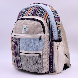 Könnte beinhalten: Beige und mehrfarbiger Rucksack mit einer Vordertasche und zwei Seitentaschen. Der Rucksack hat eine Vielzahl von Mustern, darunter Streifen und ein blaues Fischgrätendesign. Auf der Vorderseite des Rucksacks befindet sich ein kleines Etikett mit Text und einem grünen Blatt.