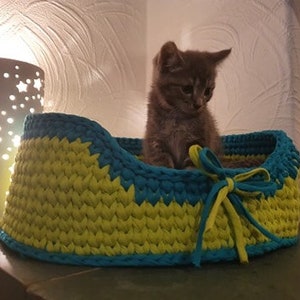 May include: A gray kitten sits in a crocheted pet bed. The bed is made of yellow and blue yarn and has a bow on the front.