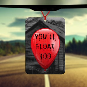 Könnte beinhalten: Roter Ballon-Lufterfrischer für das Auto mit dem Text "You'll Float Too" darauf gedruckt. Der Ballon befindet sich vor einem verschwommenen Bild eines Hauses.