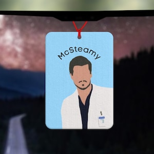 Peut inclure: Un diffuseur d'air de voiture bleu avec une illustration de dessin animé d'un homme avec une moustache et le texte "McSteamy".