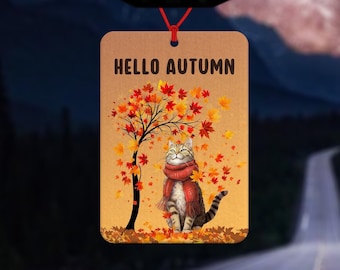 Könnte beinhalten: Ein rechteckiger Auto-Lufterfrischer mit dem Text "HELLO AUTUMN". Das Design zeigt eine getigerte Katze mit rotem Schal, die unter einem Baum mit fallenden Herbstblättern sitzt. Der Hintergrund zeigt eine verschwommene Straße.