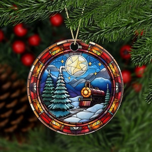 May include: Circular Christmas decoration with a stained-glass effect. It depicts a winter landscape with a train, fir trees, a full moon, and stars. The border is red, orange, and yellow. A gold string is attached for hanging.