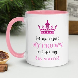 May include: White ceramic mug with a pink rim and handle. The mug features a pink crown graphic and the text "let me adjust my crown and get my day started".