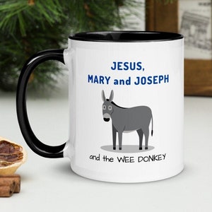 May include: White ceramic mug with a black rim and handle. The mug has a cartoon donkey and the text "JESUS, MARY and JOSEPH and the WEE DONKEY" printed on it.