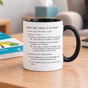 May include: A white ceramic mug with a black interior and handle, featuring black printed text that explains when sadness fits the facts, including bullet points about loss, functions, and problem-solving for justified sadness.
