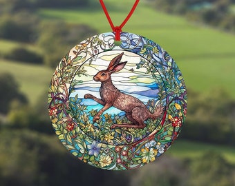 May include: A round car air freshener with a stained glass design featuring a brown rabbit in a green and blue floral setting.