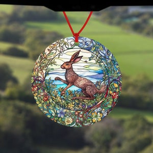 May include: A round car air freshener with a stained glass design featuring a brown rabbit in a green and blue floral setting.