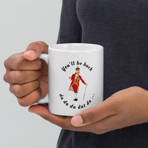 May include: White ceramic mug with a black and white illustration of a king in a red and gold costume. The text "You'll be back da da da dat da..." is printed around the illustration.