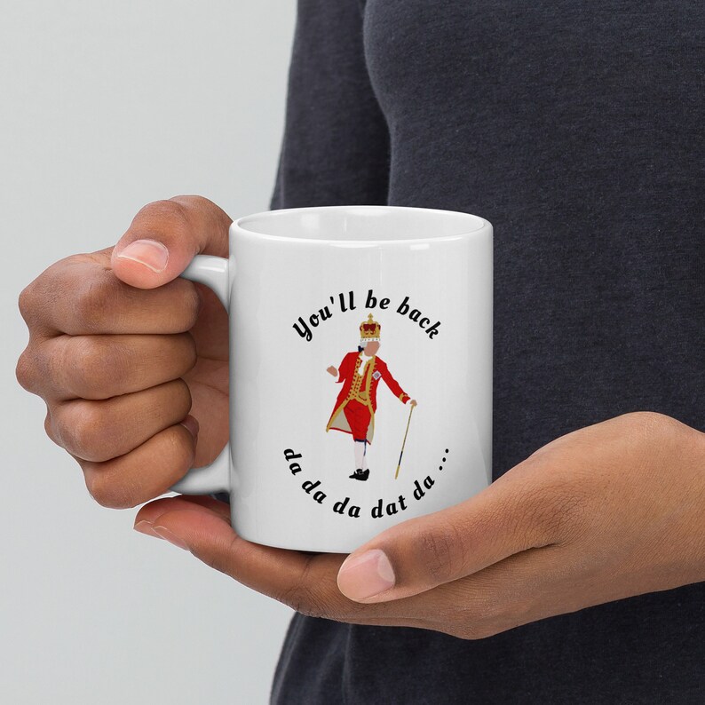 May include: White ceramic mug with a black and white illustration of a king in a red and gold costume. The text "You'll be back da da da dat da..." is printed around the illustration.