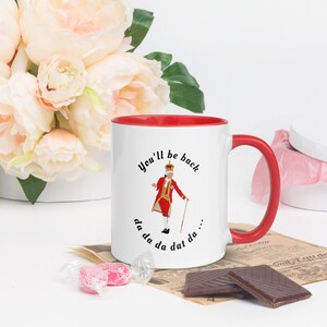 May include: White ceramic mug with a red rim and handle. The mug features a black and white illustration of a king in a red and gold costume, with the text "You'll be back da da da dat da..." printed on the mug.