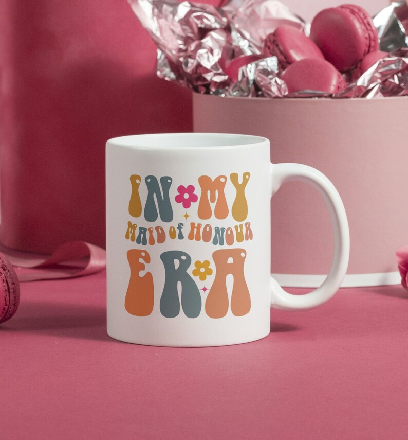 May include: White ceramic mug with a colorful graphic that says "In My Maid of Honour Era" with flowers and stars.