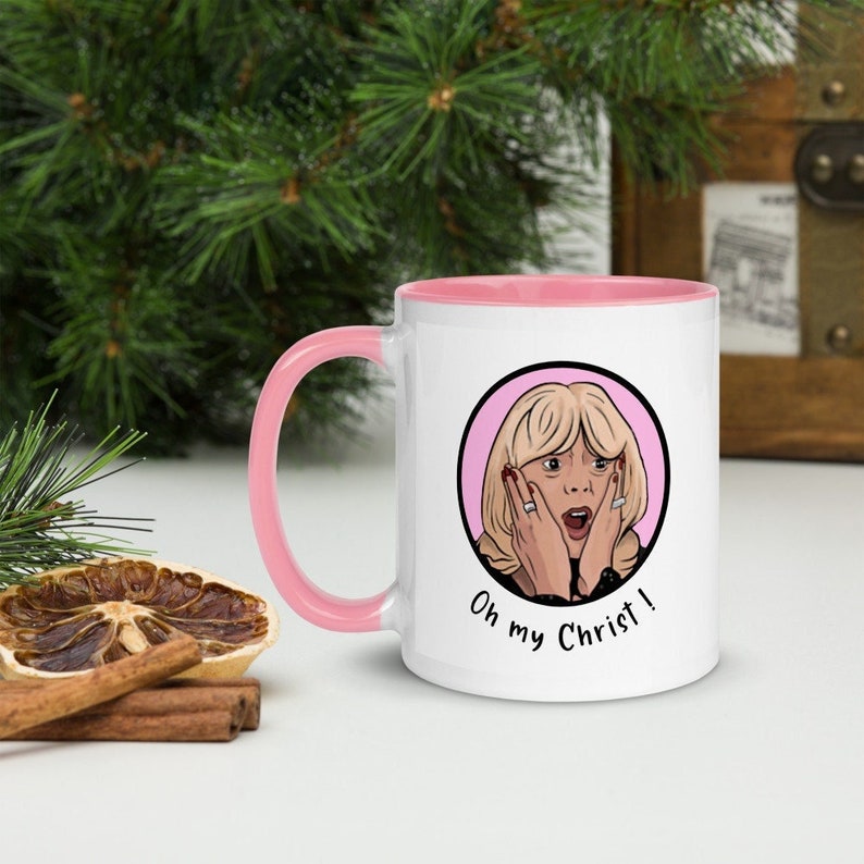 May include: White ceramic mug with a pink interior and handle. The mug features a cartoon illustration of a surprised woman with the text "Oh my Christ!" in black. The mug is set against a festive background.