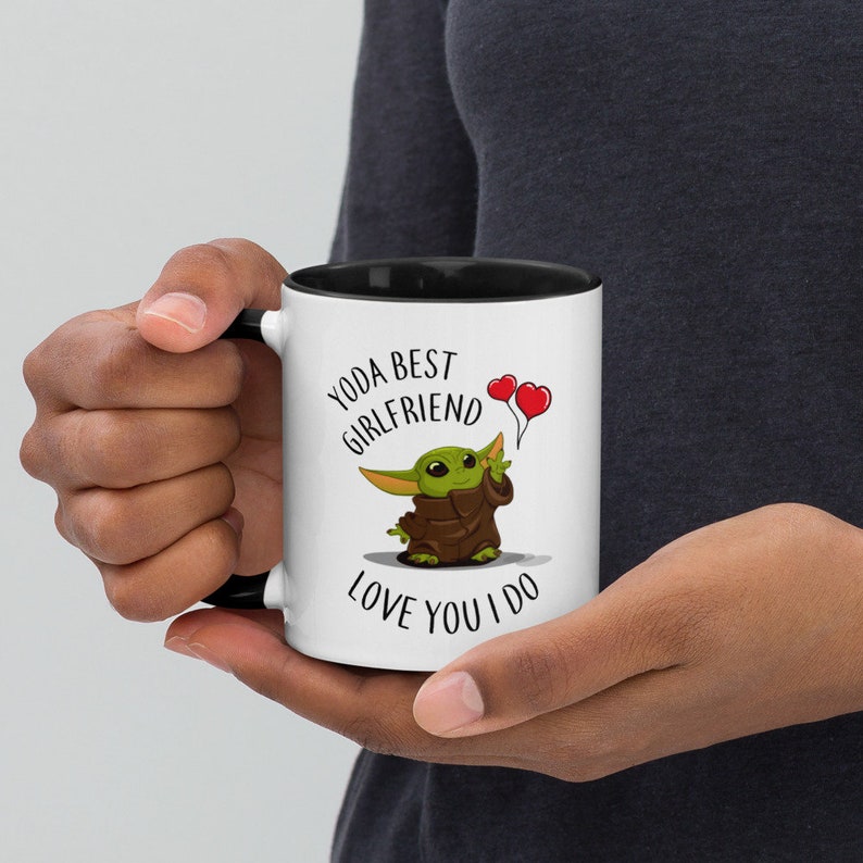 May include: White ceramic mug with a black rim and handle. The mug features a cartoon image of a green alien holding two red heart balloons. The text on the mug reads "Yoda Best Girlfriend Love You I Do."