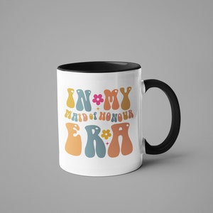 May include: White ceramic mug with a black rim and handle. The mug features a colorful retro design with the text "In My Maid of Honour Era" in a groovy font.