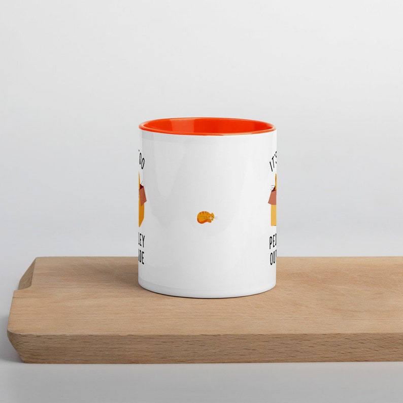 May include: White ceramic mug with an orange rim. The mug has a black and white illustration of a cat in a box with the text "It's okay to be a little crazy" on the right side and "It's perfectly normal to be a little crazy" on the left side.