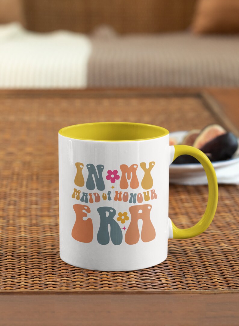 May include: White ceramic mug with a yellow rim and handle. The mug has a retro design with the text "In My Maid of Honour Era" in colorful, wavy letters.