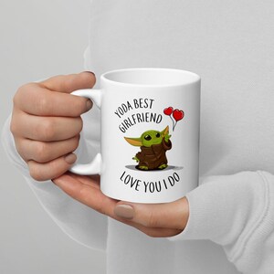 May include: White ceramic mug with a green cartoon character holding two red heart balloons. The text on the mug reads "Yoda Best Girlfriend Love You I Do."