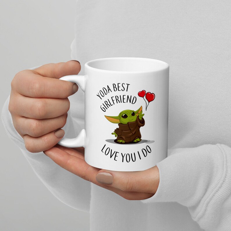 May include: White ceramic mug with a green cartoon character holding two red heart balloons. The text on the mug reads "Yoda Best Girlfriend Love You I Do."