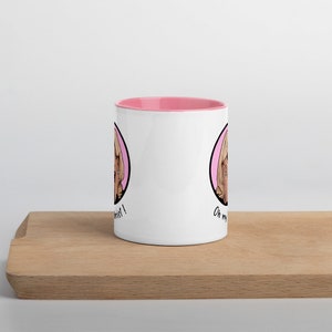 May include: White ceramic mug with a pink interior, featuring a cartoon illustration of a woman with blonde hair in a pink circle. The mug has the text "Oh my twist!" on it.