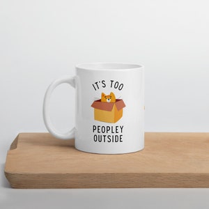 May include: White ceramic mug with a black and orange illustration of a cat in a box. The text "It's too peopley outside" is printed on the mug.