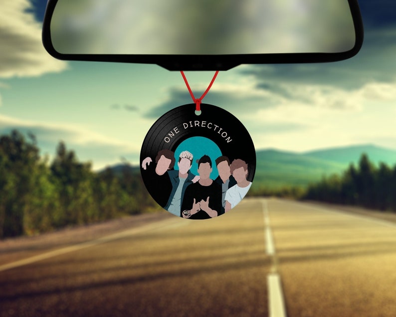 May include: Black and white car air freshener shaped like a vinyl record with a picture of five men and the text "One Direction" on it.